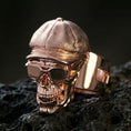 Load image into Gallery viewer, Sterling silver skull ring with a rose gold plated finish, sculpted cap and glasses details, close-up on black volcanic rock
