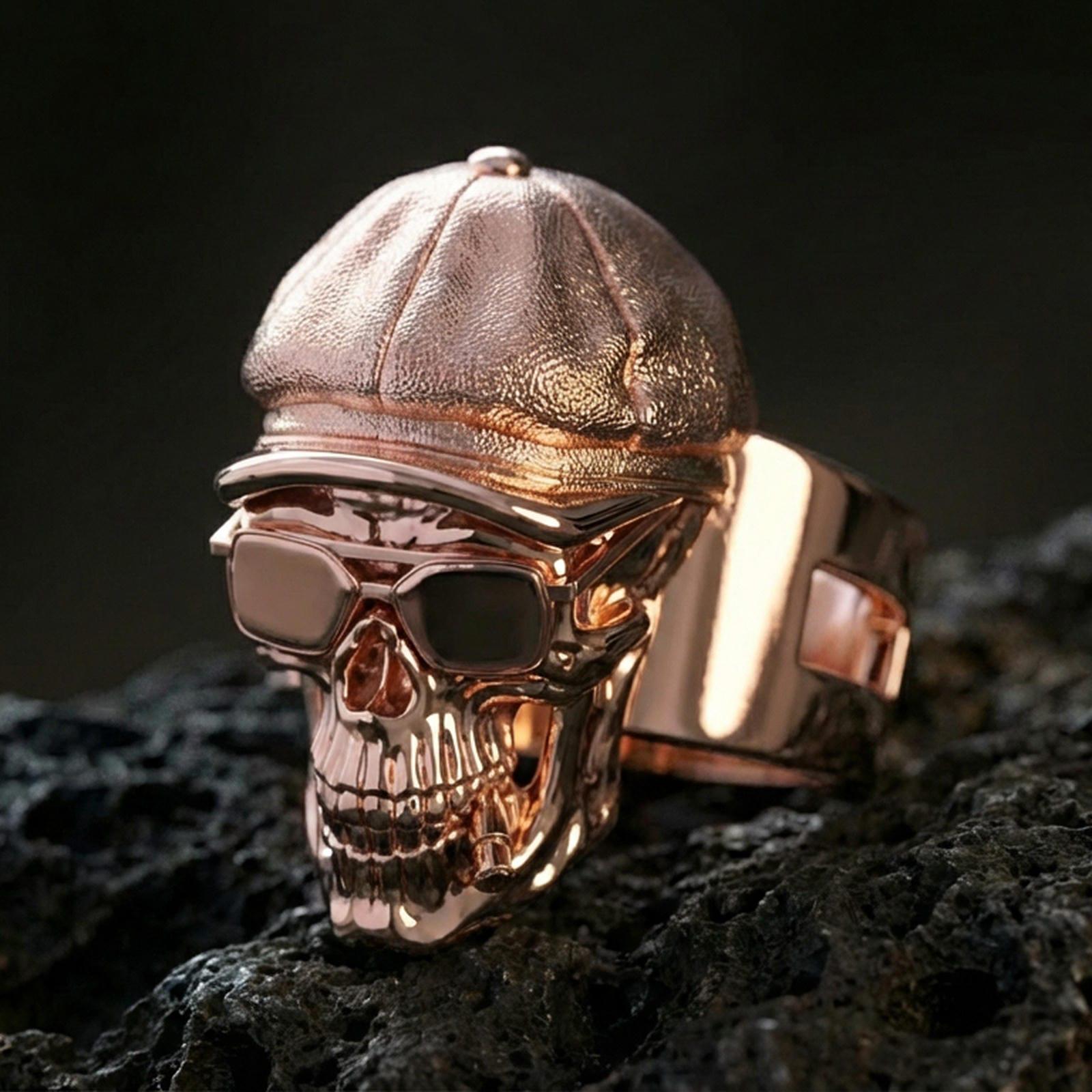 Sterling silver skull ring with a rose gold plated finish, sculpted cap and glasses details, close-up on black volcanic rock