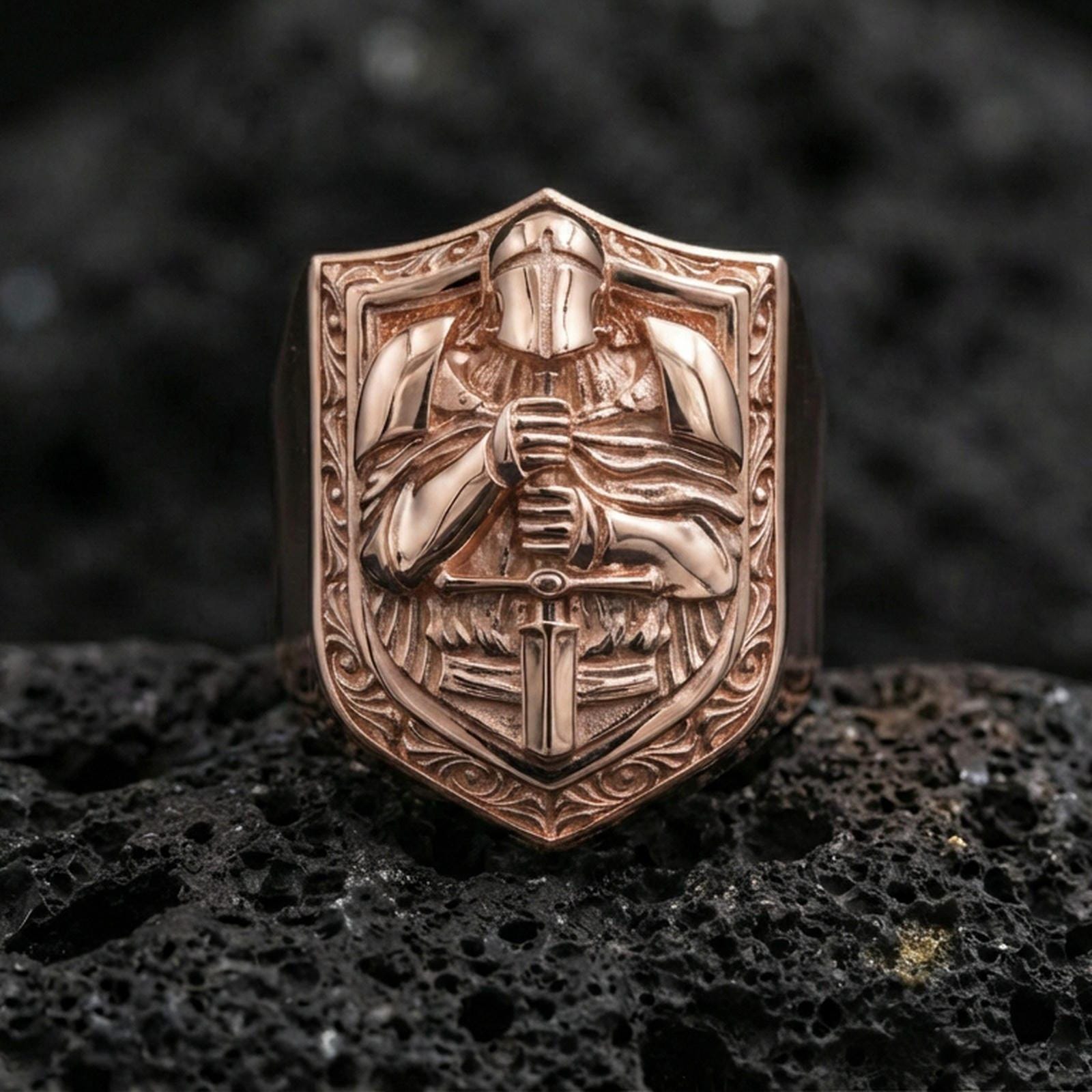 Sterling silver knight signet ring with a rose gold plated finish, medieval armored warrior on shield face with ornate border, macro on volcanic rock