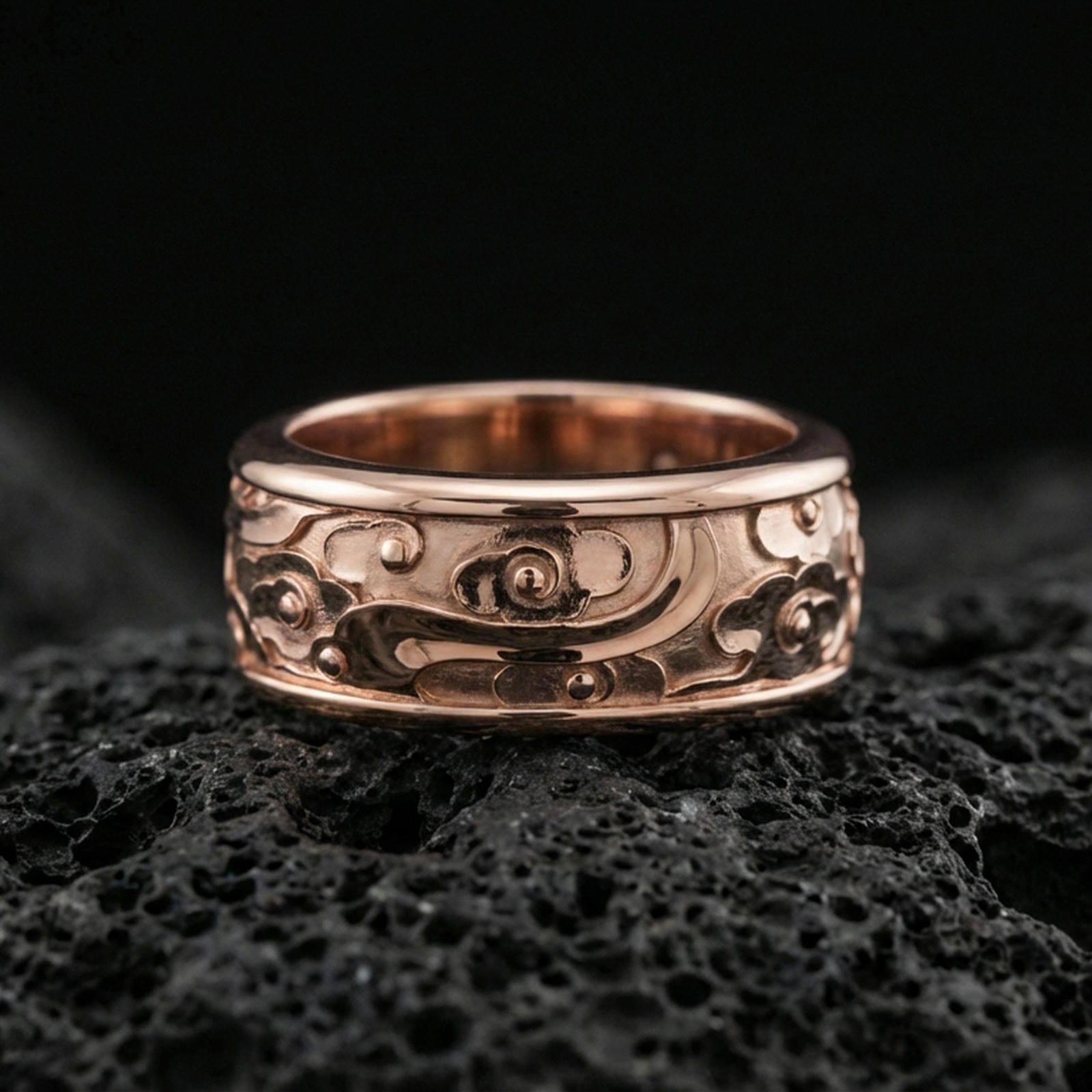 Rose gold plated sterling silver spinner cloud band on volcanic stone, playful swirl relief with floral accents and deep contrast, minimal high-end close-up.