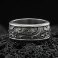 Load image into Gallery viewer, Oxidized sterling silver spinning cloud band ring on dark volcanic rock, whimsical swirl and flower relief on rotating center, premium macro product shot.
