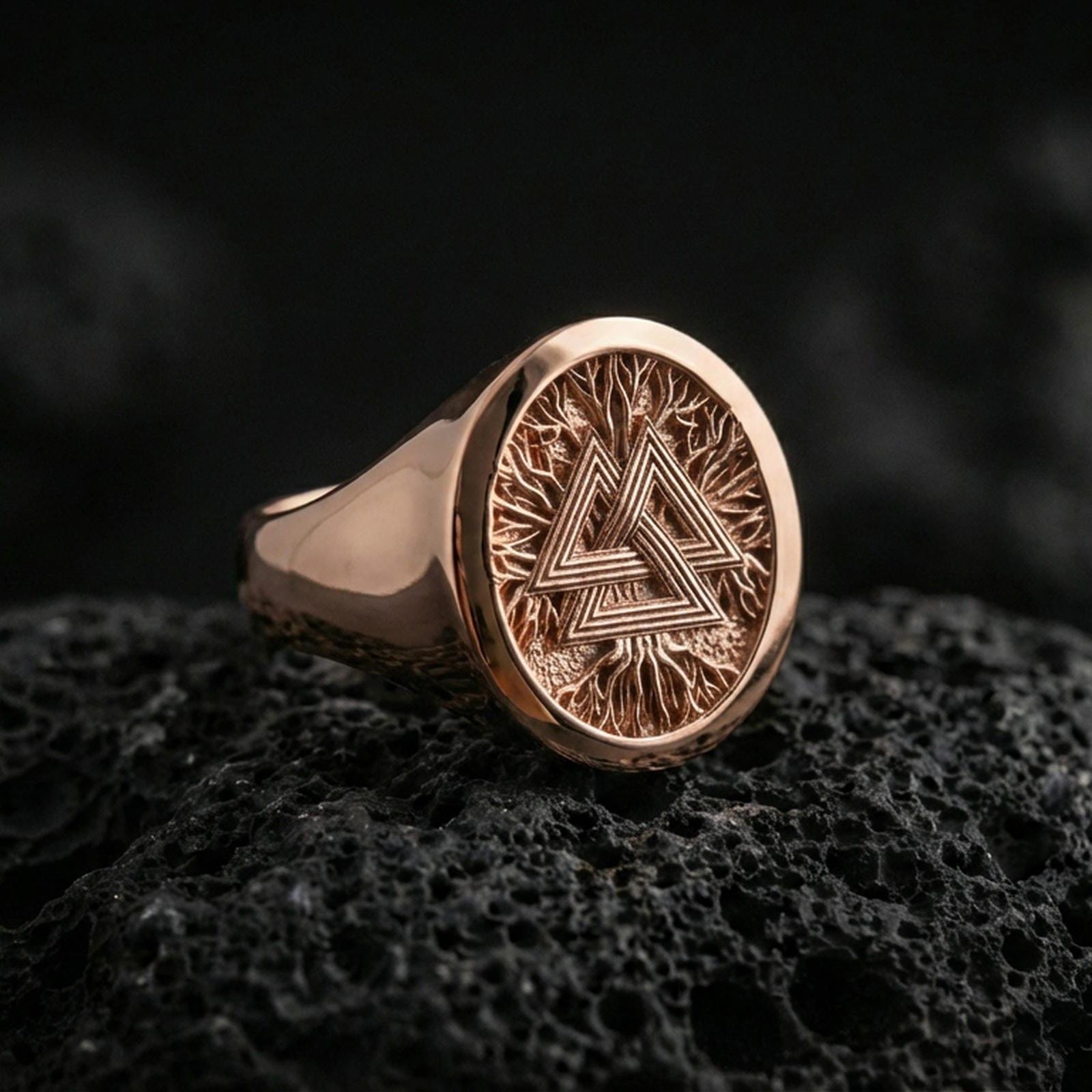 Sterling silver Valknut signet ring with a rose gold plated finish, circular signet face with the Norse Valknut symbol and detailed etched texture, close-up on volcanic rock