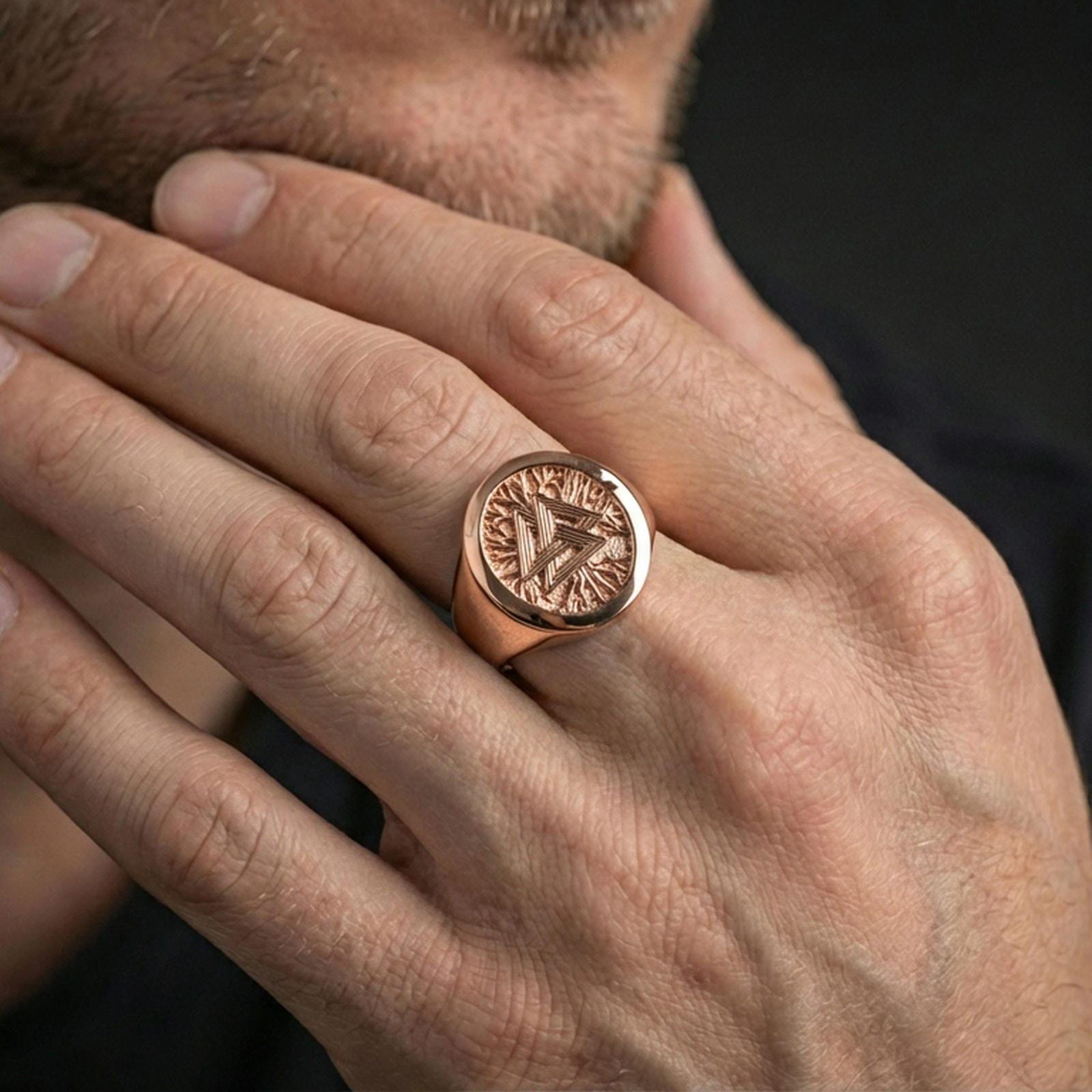 Rose gold plated finish Valknut signet ring on the finger, macro lifestyle shot showcasing the round frame and engraved Viking texture details