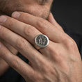 Load image into Gallery viewer, Oxidized finish Valknut signet ring worn on a finger, round face with Norse triple triangle symbol shown in a close-up lifestyle shot
