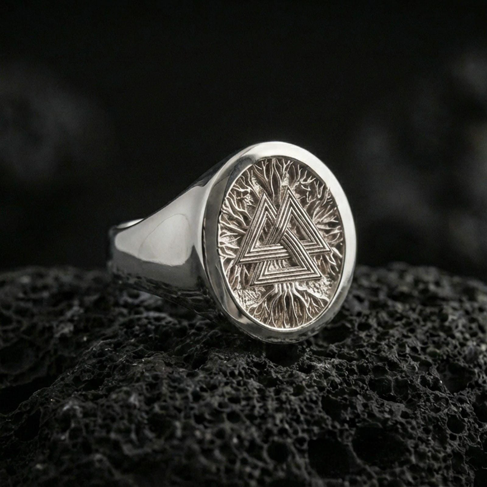 Sterling silver Valknut signet ring in a polished silver finish, circular signet face with the Valknut symbol and engraved root pattern, close-up on volcanic stone