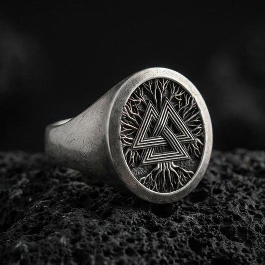 Sterling silver Valknut signet ring with an oxidized finish, round face featuring a Norse triple-triangle symbol over a branch-like texture, macro on black volcanic rock
