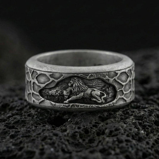 Oxidized sterling silver spinning lion band ring on dark volcanic rock, engraved lion scene on rotating center with textured border, premium macro product shot.