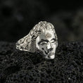 Load image into Gallery viewer, Sterling silver third eye face ring in a polished silver finish, raised mask profile with forehead eye symbol and ornate side engravings, close-up on volcanic stone
