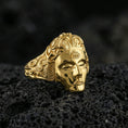 Load image into Gallery viewer, Sterling silver third eye face ring with a gold plated finish, serene mask design featuring a forehead eye motif and detailed scrollwork band, macro on volcanic rock
