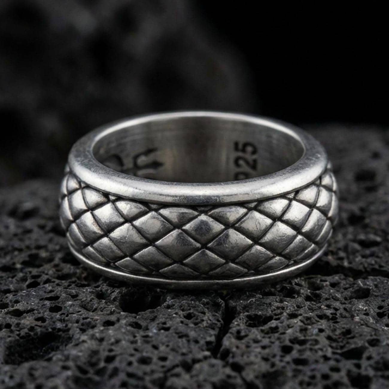 Oxidized sterling silver quilted diamond texture band ring on dark volcanic rock, raised pillow pattern detail, premium macro product shot.