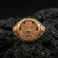 Load image into Gallery viewer, Sterling silver US eagle seal signet ring with a rose gold plated finish, detailed eagle emblem signet face with vintage-style engraving, close-up on volcanic rock
