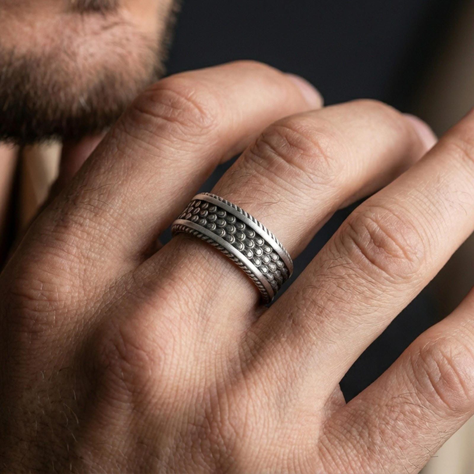 Oxidized sterling silver beaded dot texture band worn on finger, bubble pattern detail with rope edge border, natural lifestyle hand shot with shallow depth of field.