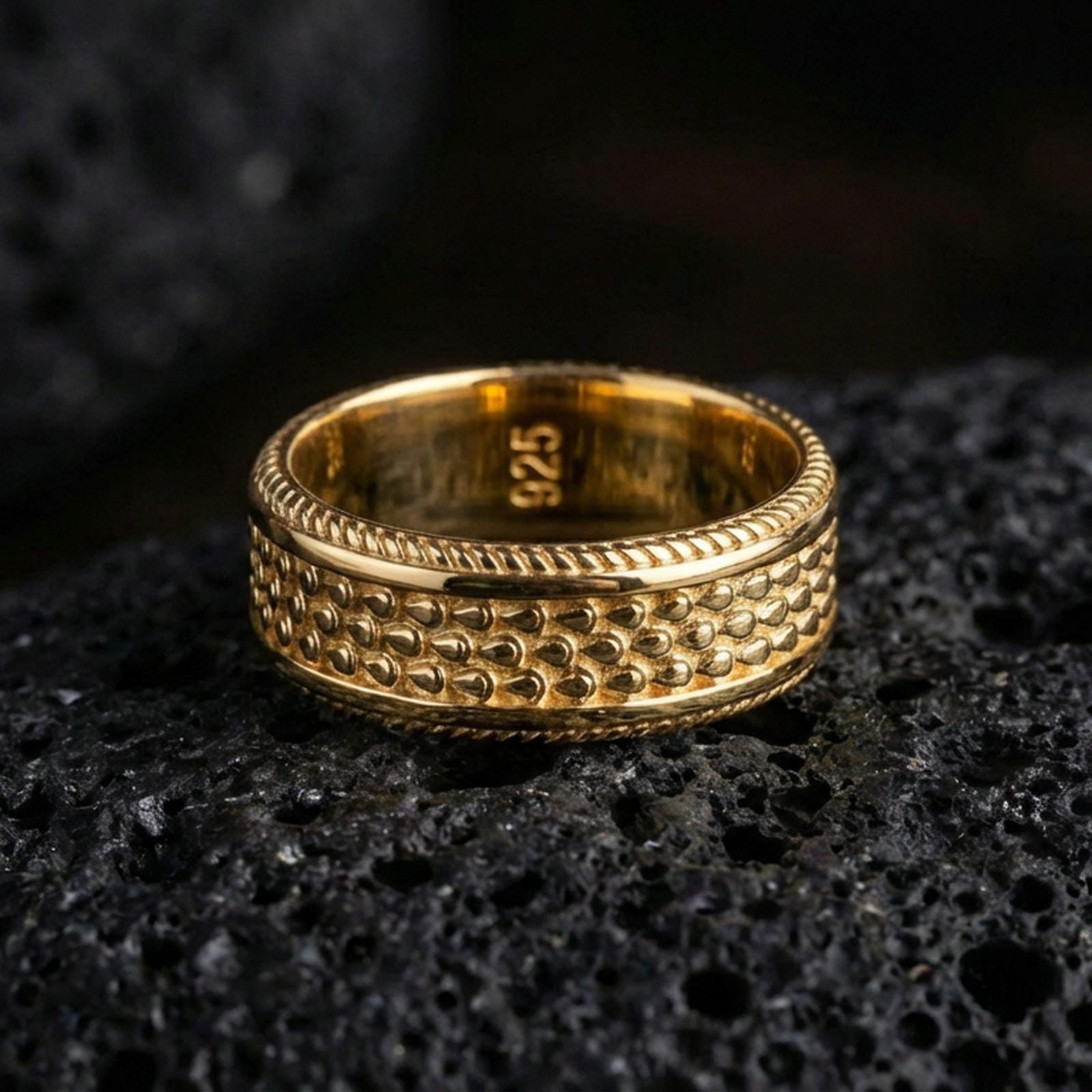 Gold plated beaded dot pattern band ring on volcanic rock, detailed bubble texture with rope edge trim, luxury jewelry product photography.