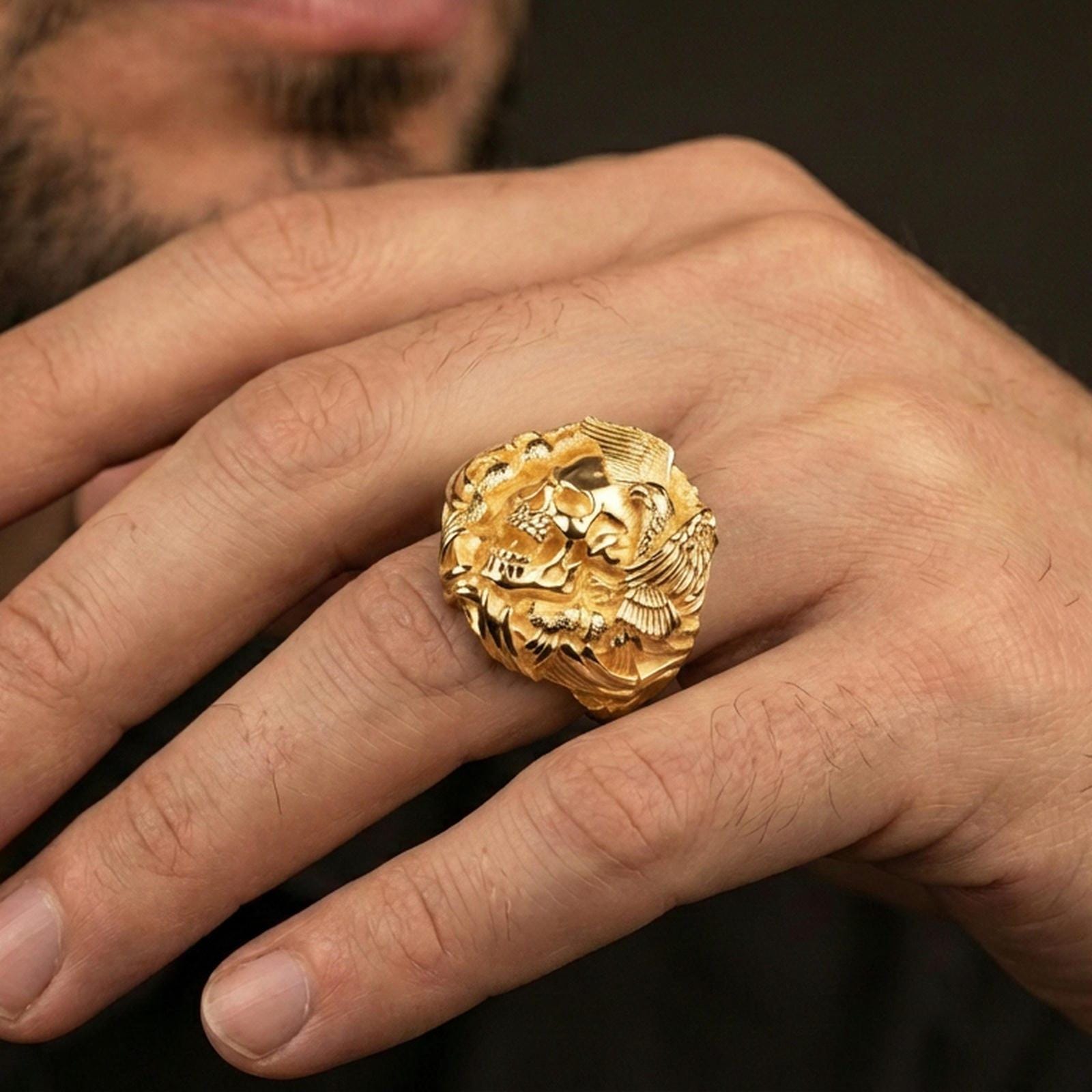 Gold plated finish skull and eagle ring worn on a finger, close-up lifestyle photo focusing on the gothic skull centerpiece and bold shine