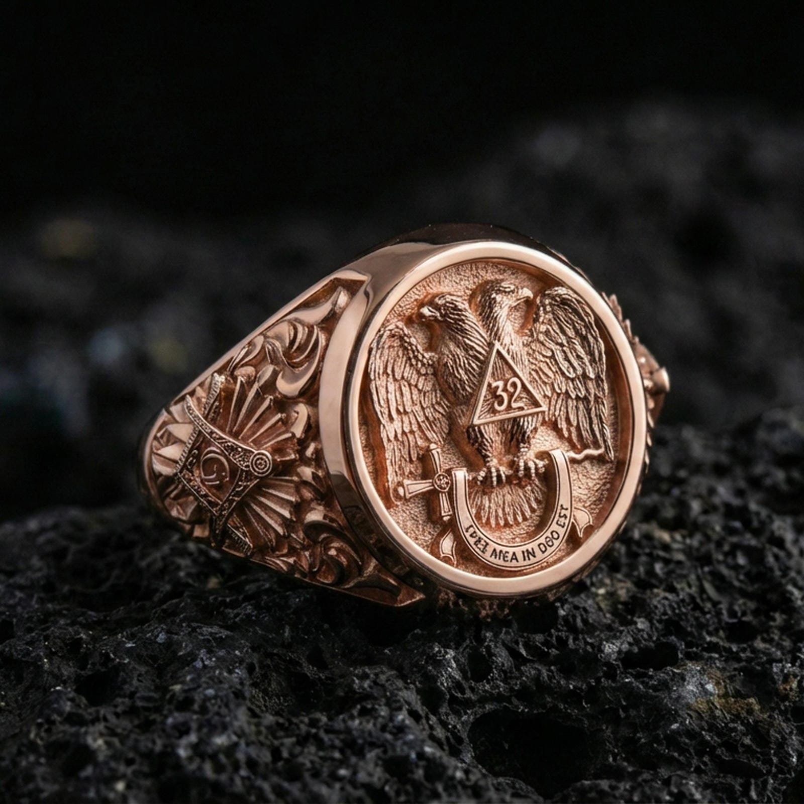 Sterling silver Masonic ring with a rose gold plated finish, detailed double-headed eagle crest and Masonic side symbol engraving, close-up on volcanic rock