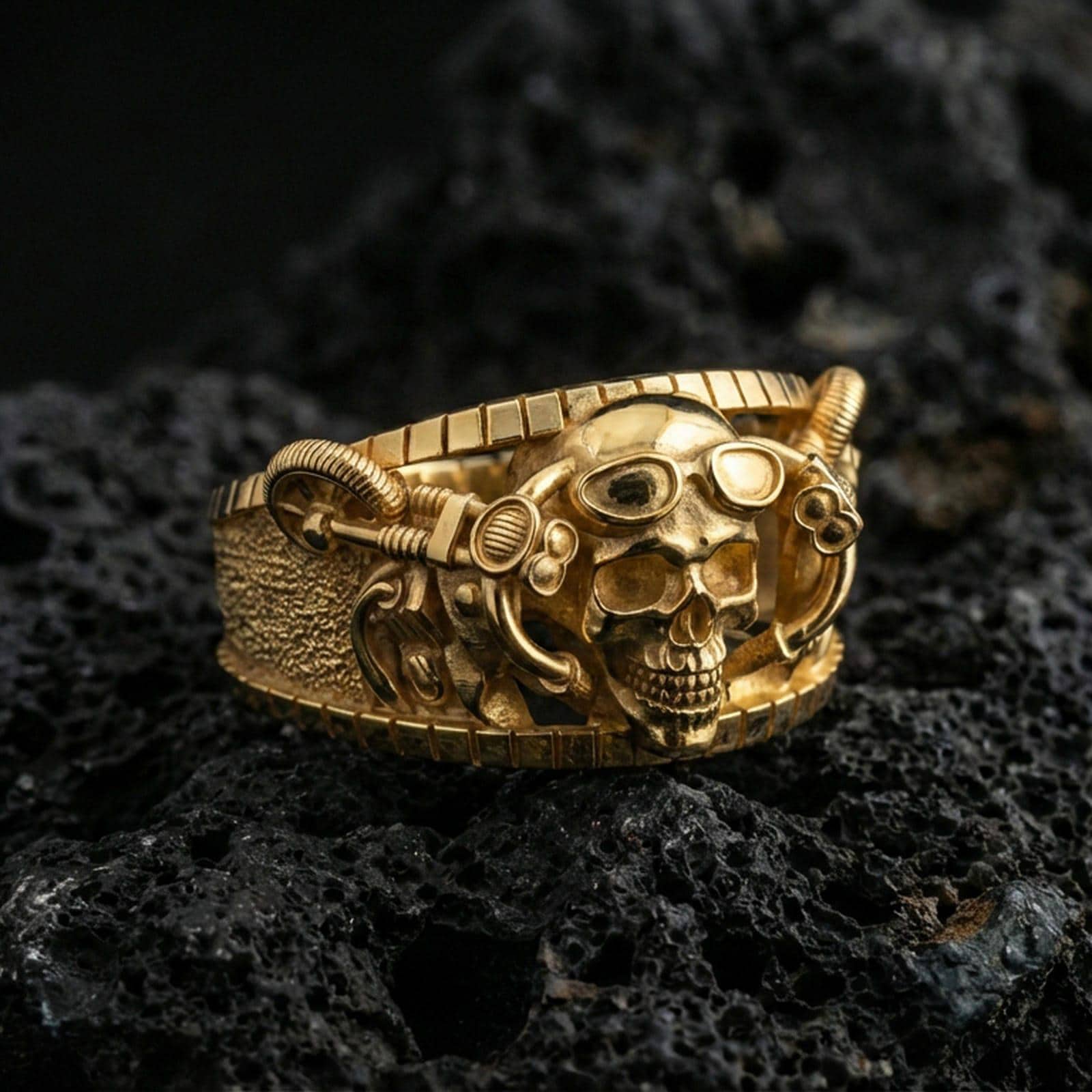 Gold plated steampunk skull ring on volcanic rock, detailed goggles and industrial hardware accents, luxury jewelry product photography.