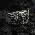 Load image into Gallery viewer, Oxidized sterling silver steampunk skull ring on dark volcanic rock, goggles and mechanical tubing detail, premium macro product shot.
