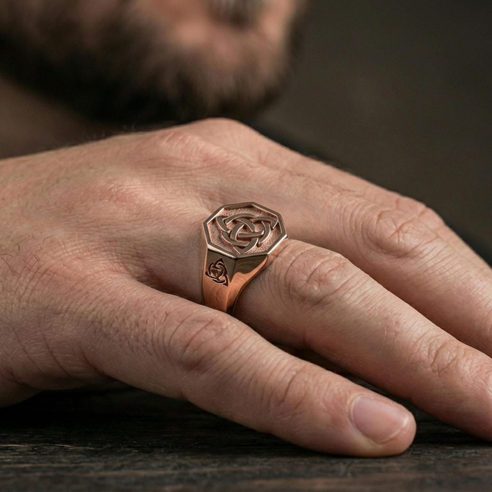 Rose gold plated finish triquetra Celtic knot signet ring on the finger, macro lifestyle shot focusing on the raised knot symbol and smooth band