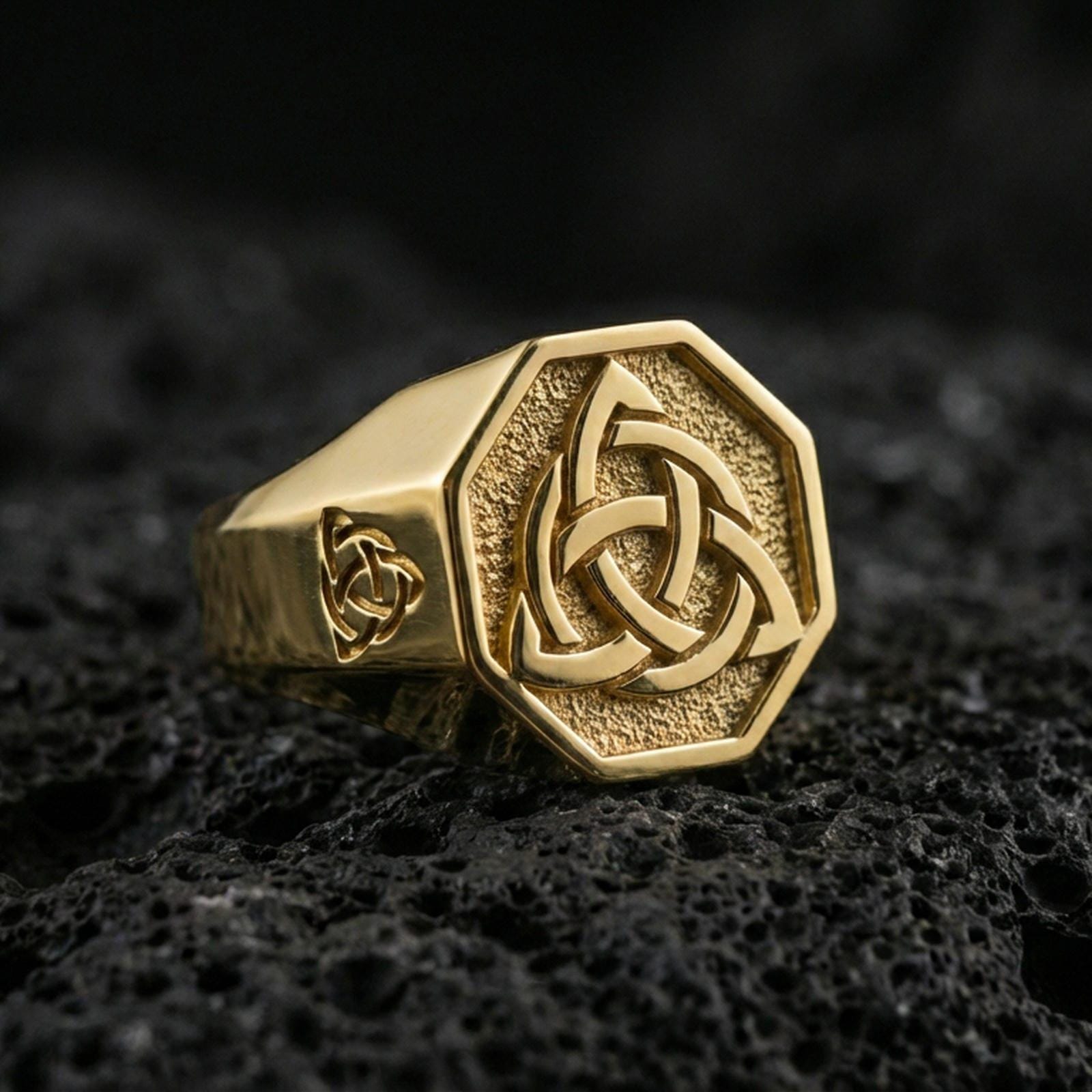 Sterling silver triquetra signet ring with a gold plated finish, raised Celtic knot on octagonal signet face, macro on volcanic rock
