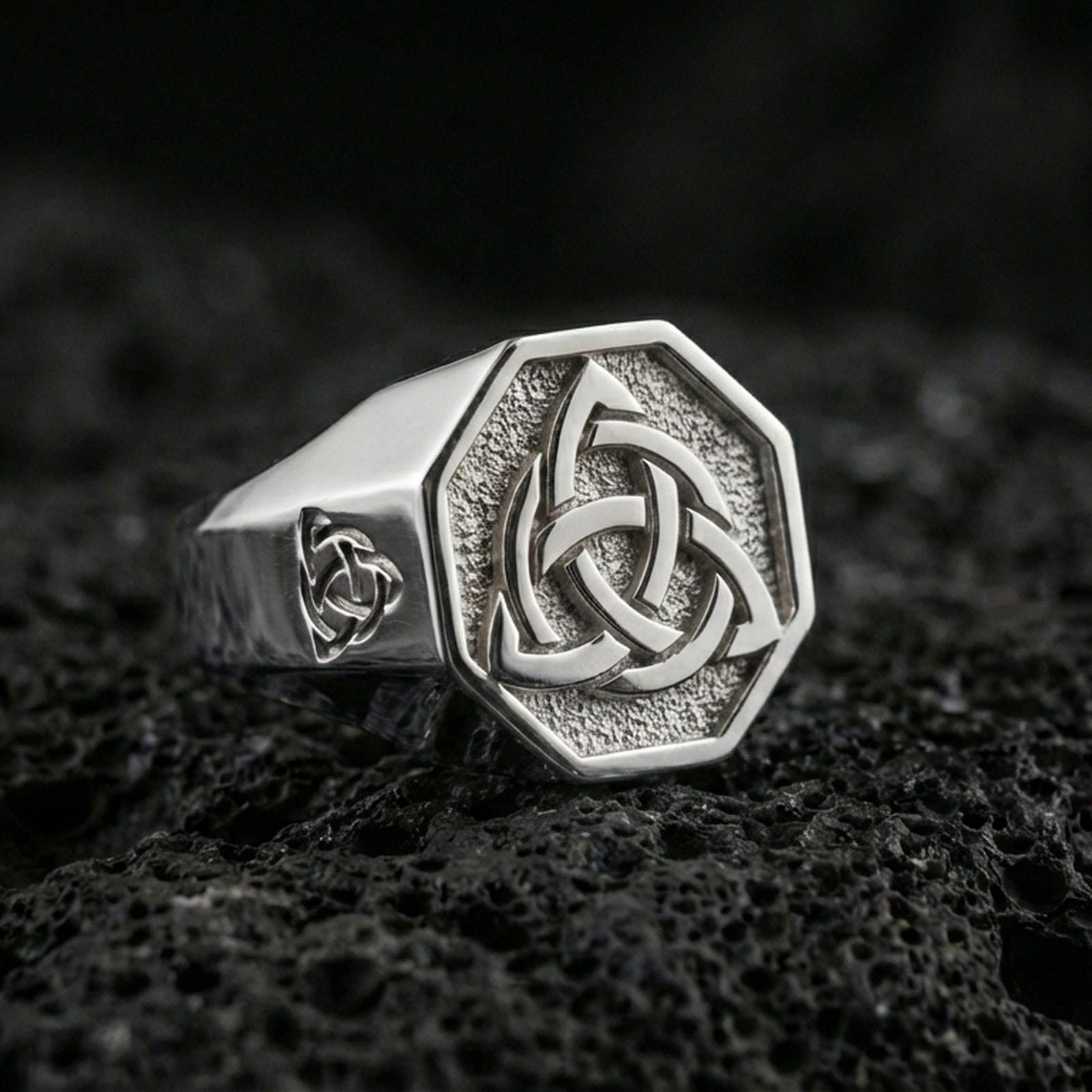 Sterling silver triquetra signet ring in a polished silver finish, octagon signet face with crisp Celtic trinity knot, close-up on volcanic stone