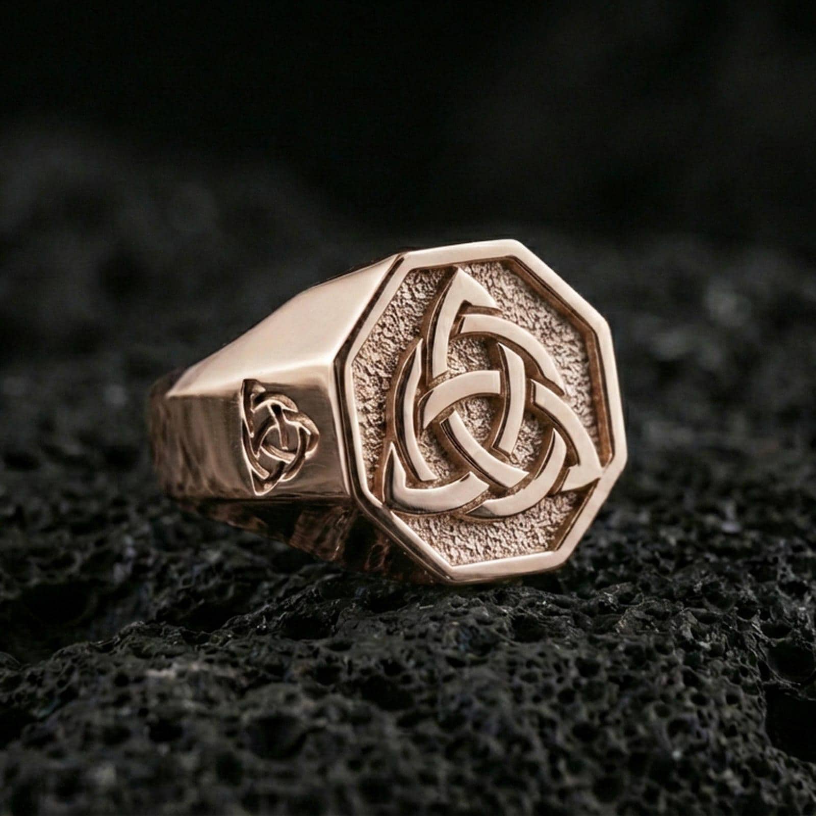 Sterling silver triquetra signet ring with a rose gold plated finish, octagon signet face featuring a triquetra Celtic knot, close-up on volcanic rock
