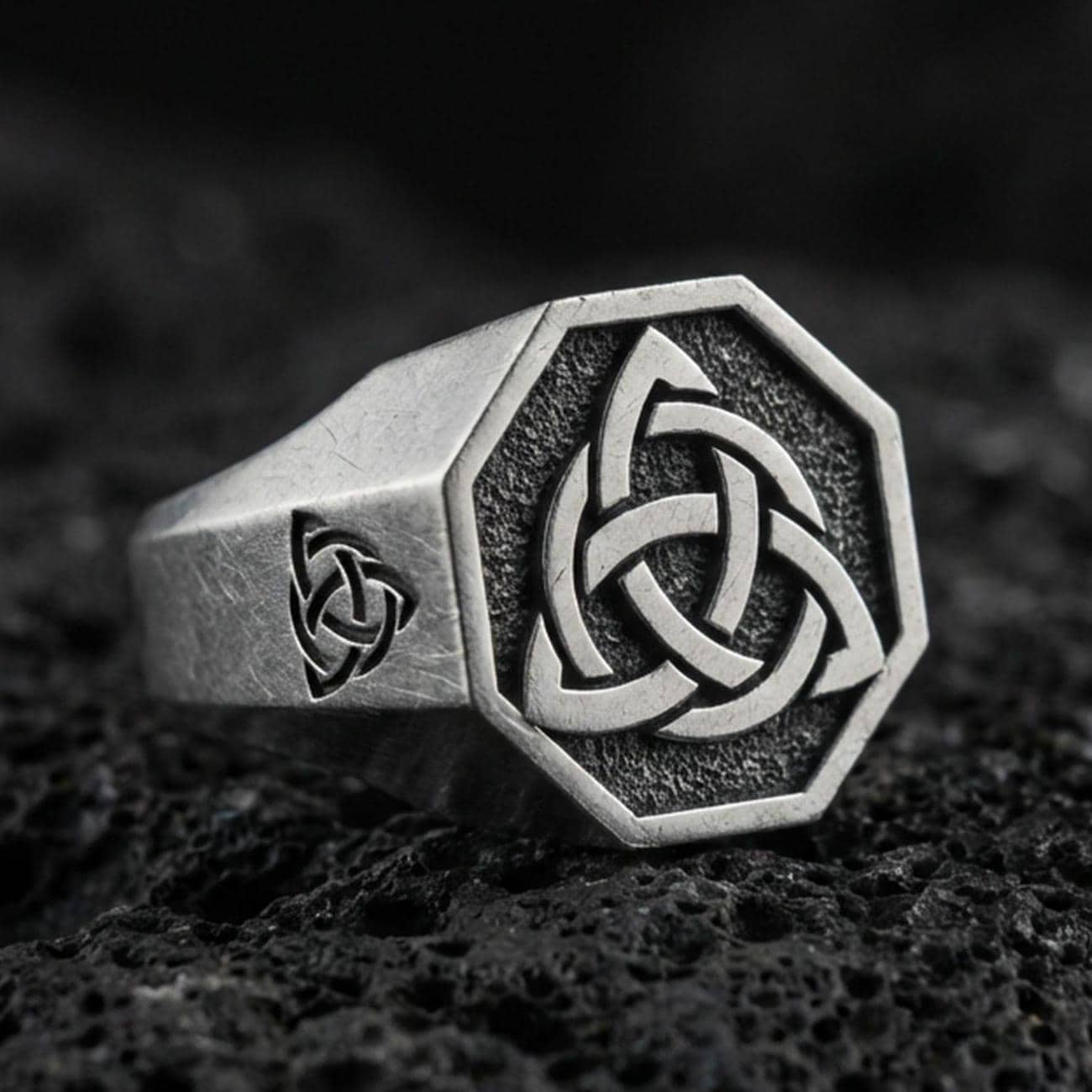 Sterling silver triquetra signet ring with an oxidized finish, octagonal face and Celtic knot symbol, macro on black volcanic rock