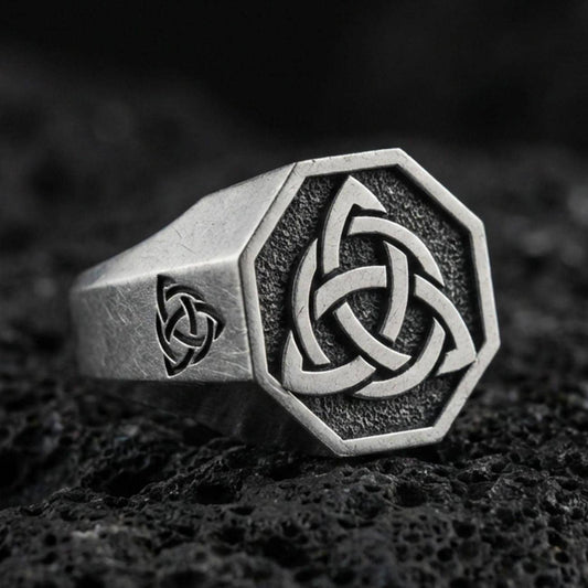 Sterling silver triquetra signet ring with an oxidized finish, octagonal face and Celtic knot symbol, macro on black volcanic rock