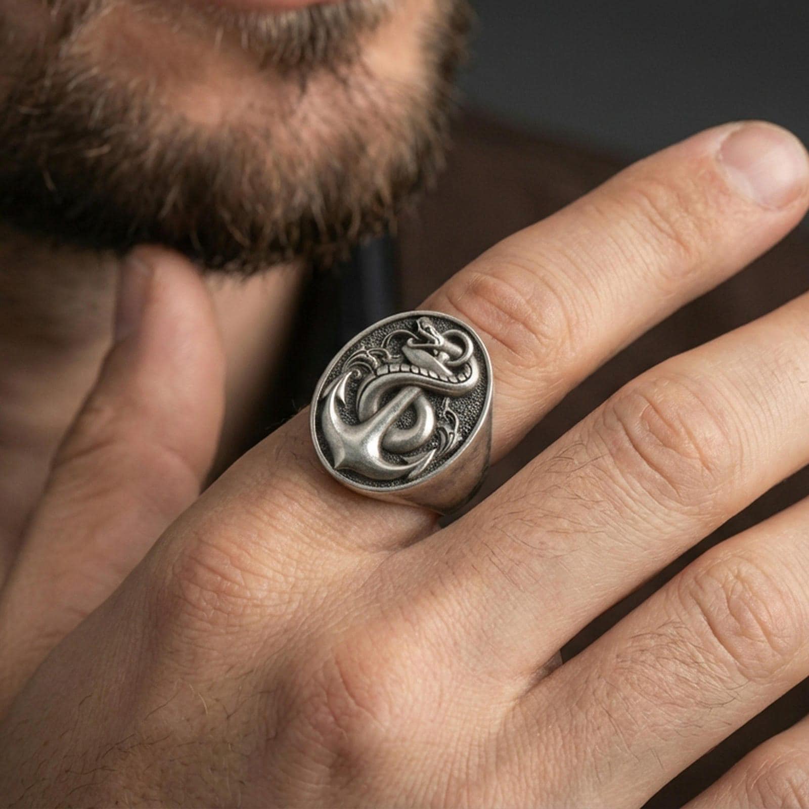 Oxidized finish sterling silver anchor and snake signet ring worn on a finger, close-up lifestyle shot highlighting the nautical emblem and relief depth