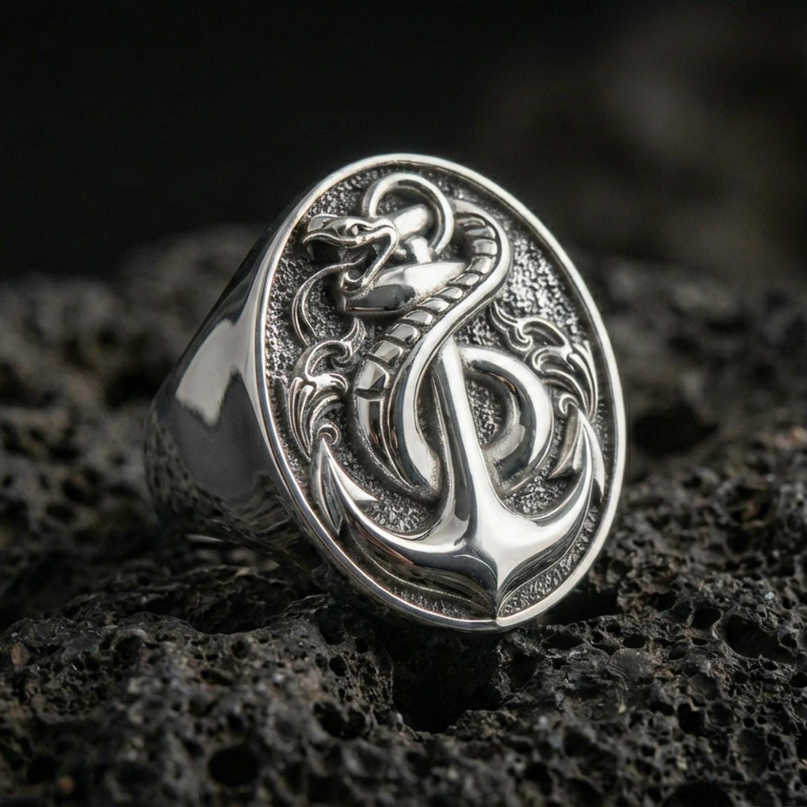 Sterling silver anchor and snake signet ring in a polished silver finish, detailed nautical anchor motif with coiled serpent, close-up on volcanic stone