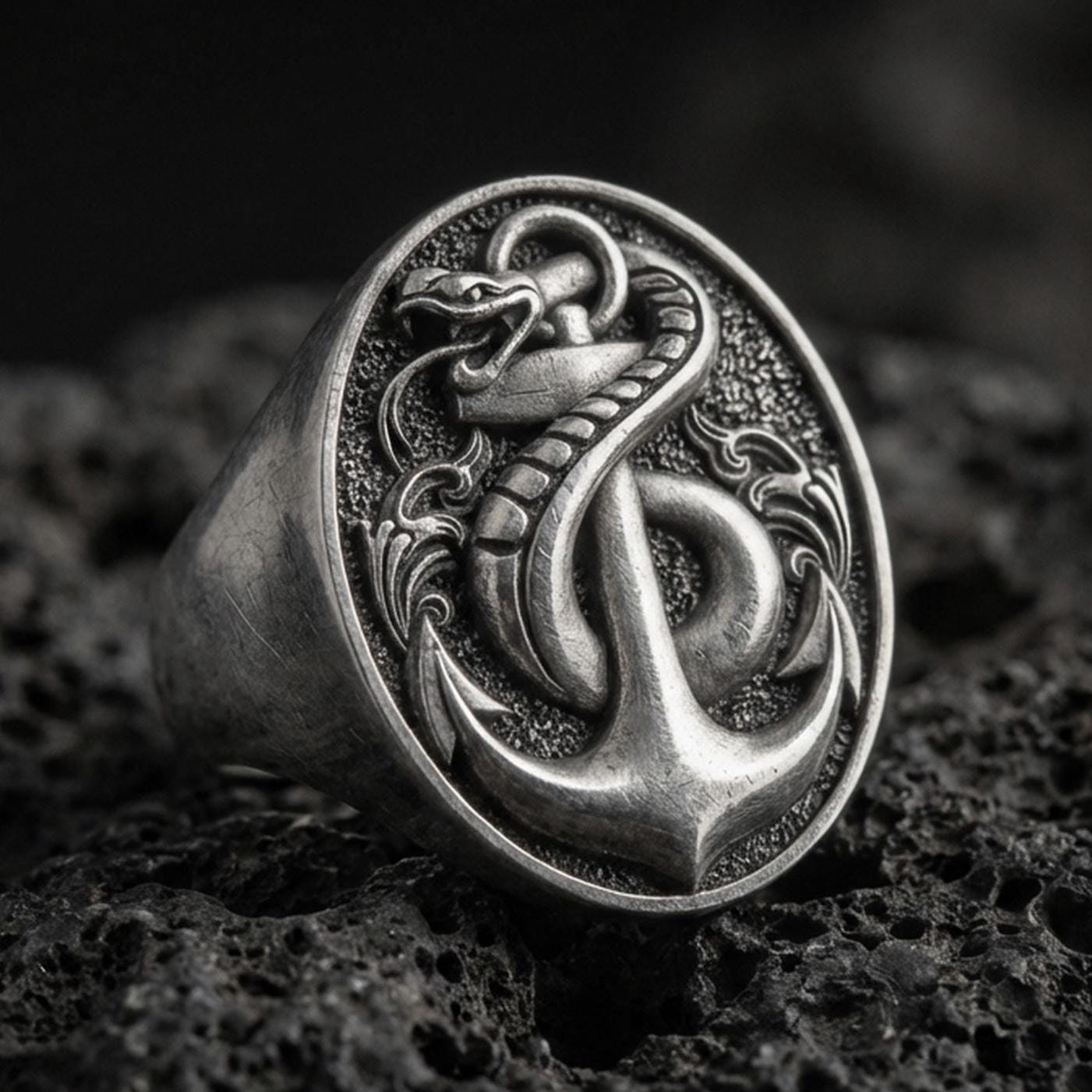 Sterling silver anchor and snake signet ring with an oxidized finish, nautical serpent emblem in high relief, macro on black volcanic rock