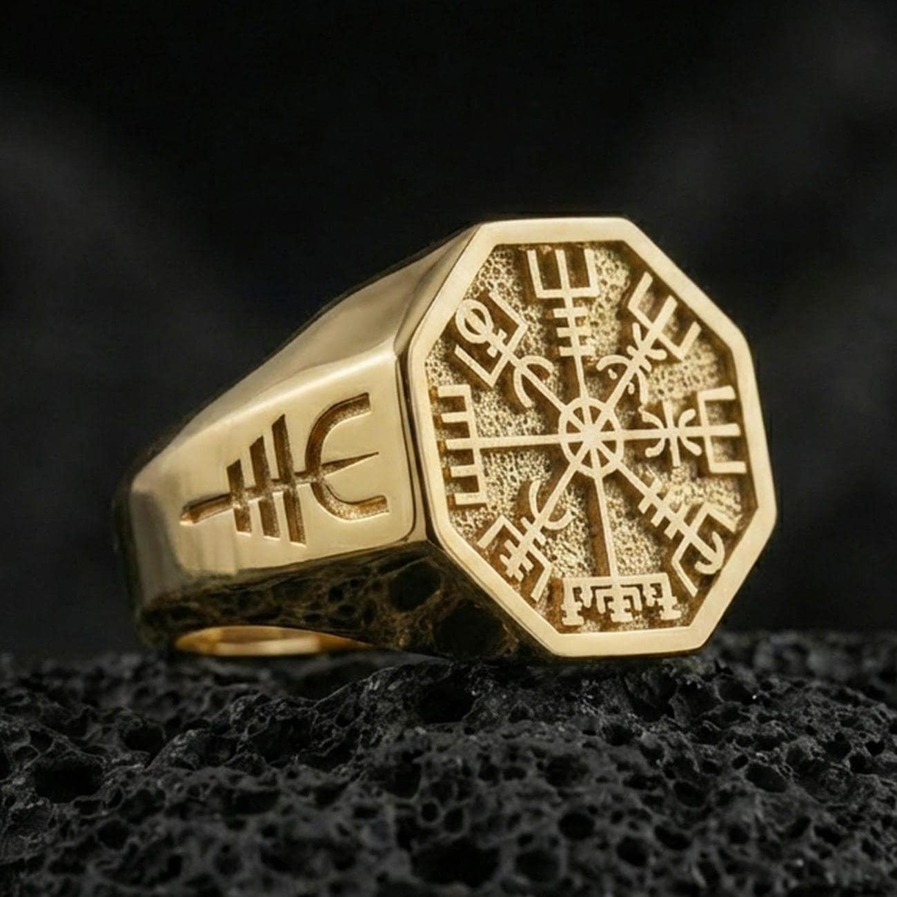 Sterling silver Vegvisir signet ring with a gold plated finish, Viking runic compass design on an octagonal face, macro on volcanic rock