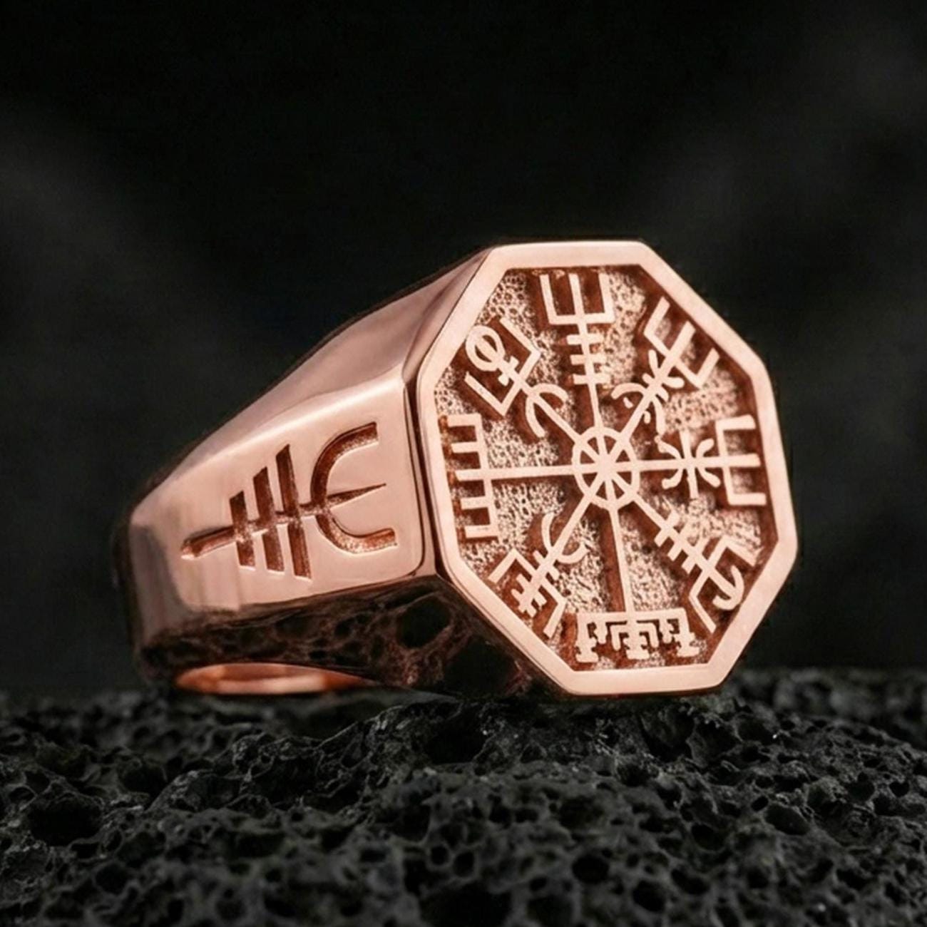 Sterling silver Vegvisir signet ring with a rose gold plated finish, Norse Vegvisir compass emblem engraved in high contrast, close-up on volcanic rock