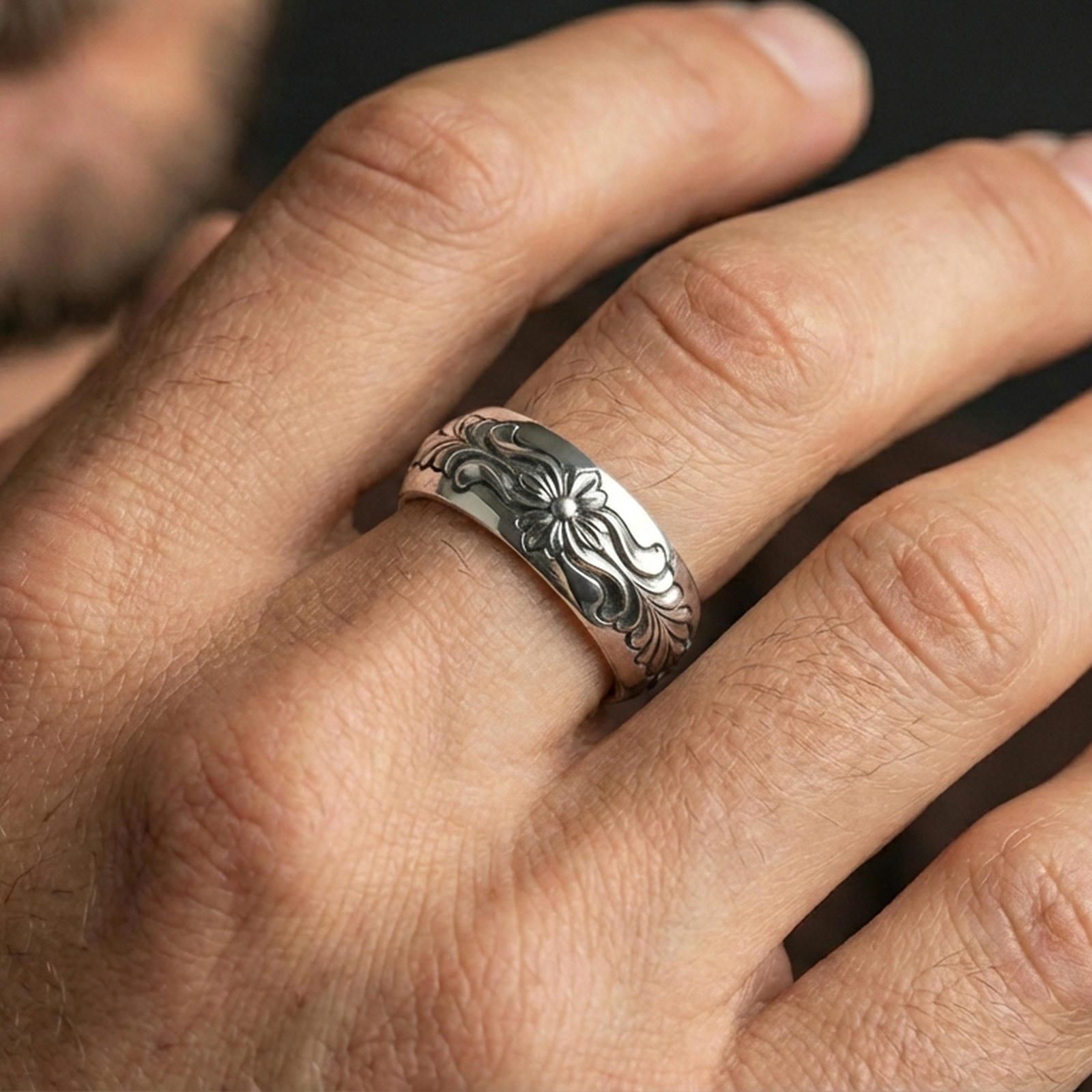Polished silver floral engraved band ring on finger, crisp flower relief and smooth scrollwork detail, refined everyday wear close-up.