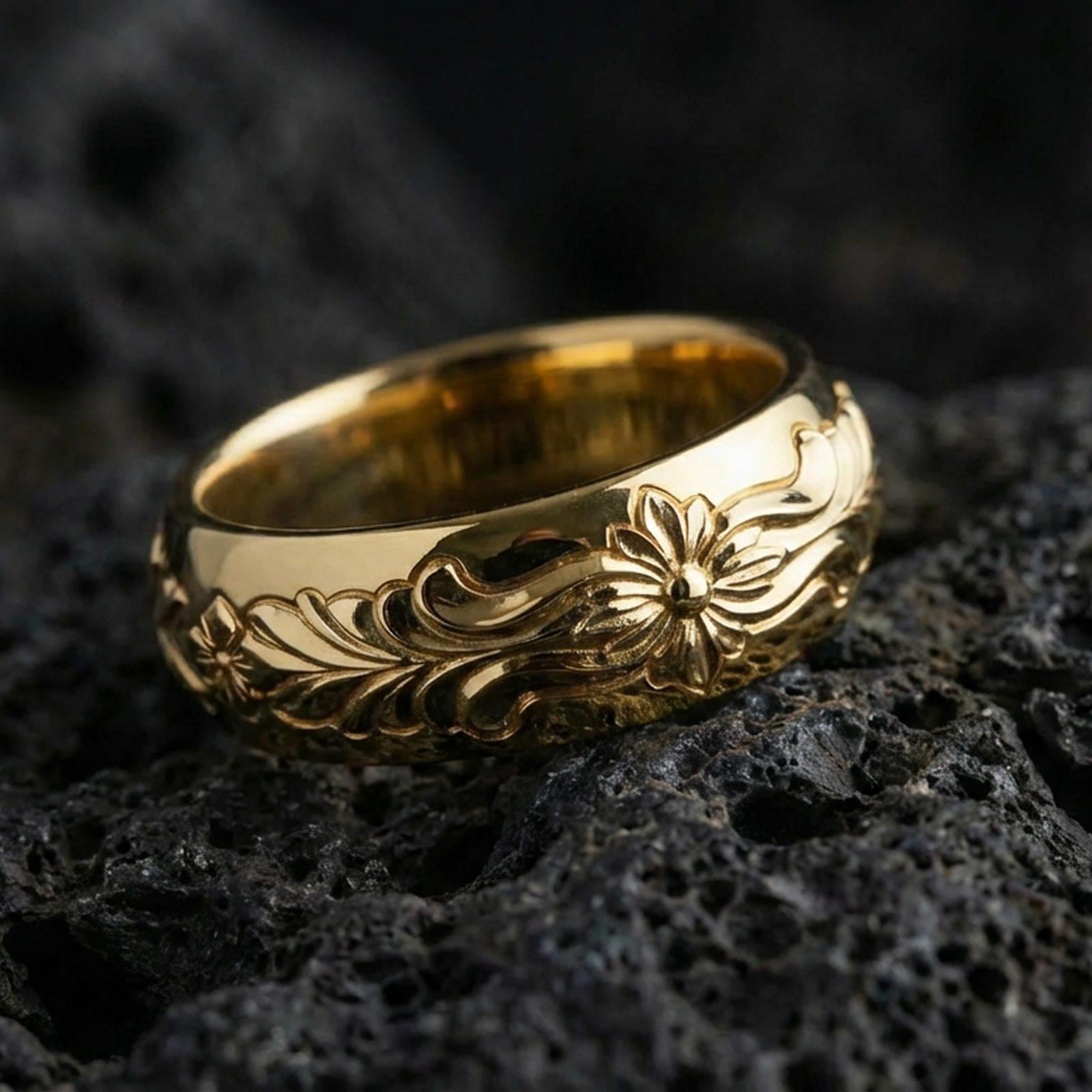 Gold plated floral scroll band ring on volcanic rock, detailed raised flower and elegant leaf engraving, luxury jewelry product photography.