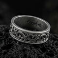 Load image into Gallery viewer, Oxidized sterling silver scrollwork band ring on dark volcanic rock, ornate swirl engraving with beaded borders, premium macro product shot.
