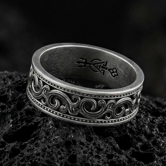 Oxidized sterling silver scrollwork band ring on dark volcanic rock, ornate swirl engraving with beaded borders, premium macro product shot.