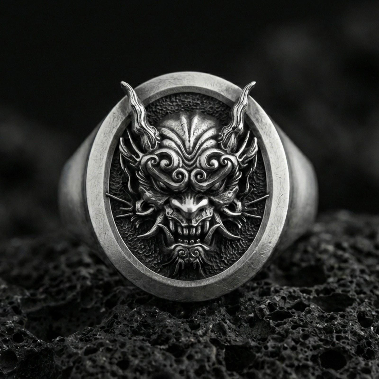Oxidized sterling silver oni mask signet ring on porous volcanic rock, macro view showing high relief facial details