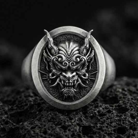 Oxidized sterling silver oni mask signet ring on porous volcanic rock, macro view showing high relief facial details