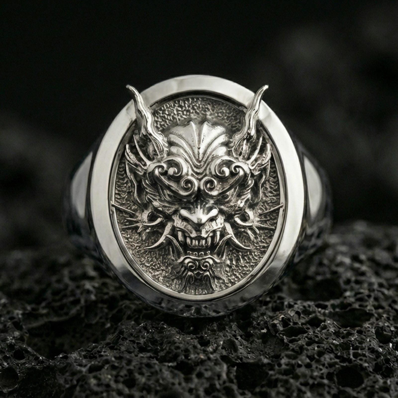 Polished silver Japanese demon ring on volcanic stone, close-up highlighting engraved textures and bold signet face