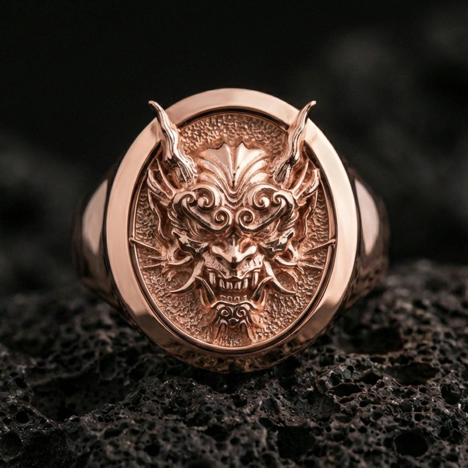 Rose gold plated Japanese demon signet ring on porous volcanic rock, premium lighting emphasizing depth and contrast