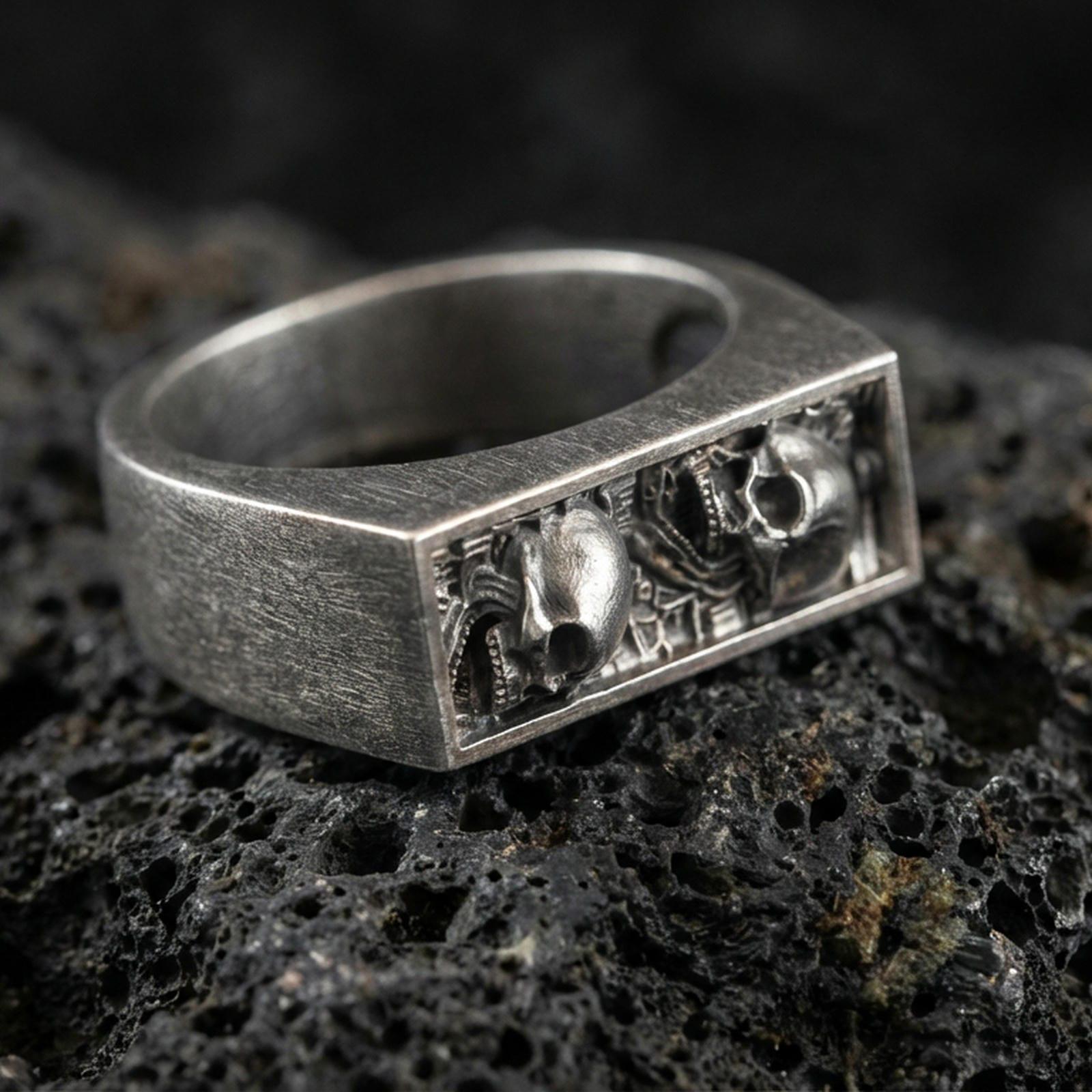 Sterling silver minimalist signet ring with an oxidized finish, rectangular open-window detail with sculpted skull accents, macro on black volcanic rock