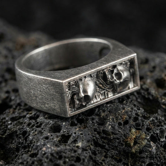 Sterling silver minimalist signet ring with an oxidized finish, rectangular open-window detail with sculpted skull accents, macro on black volcanic rock