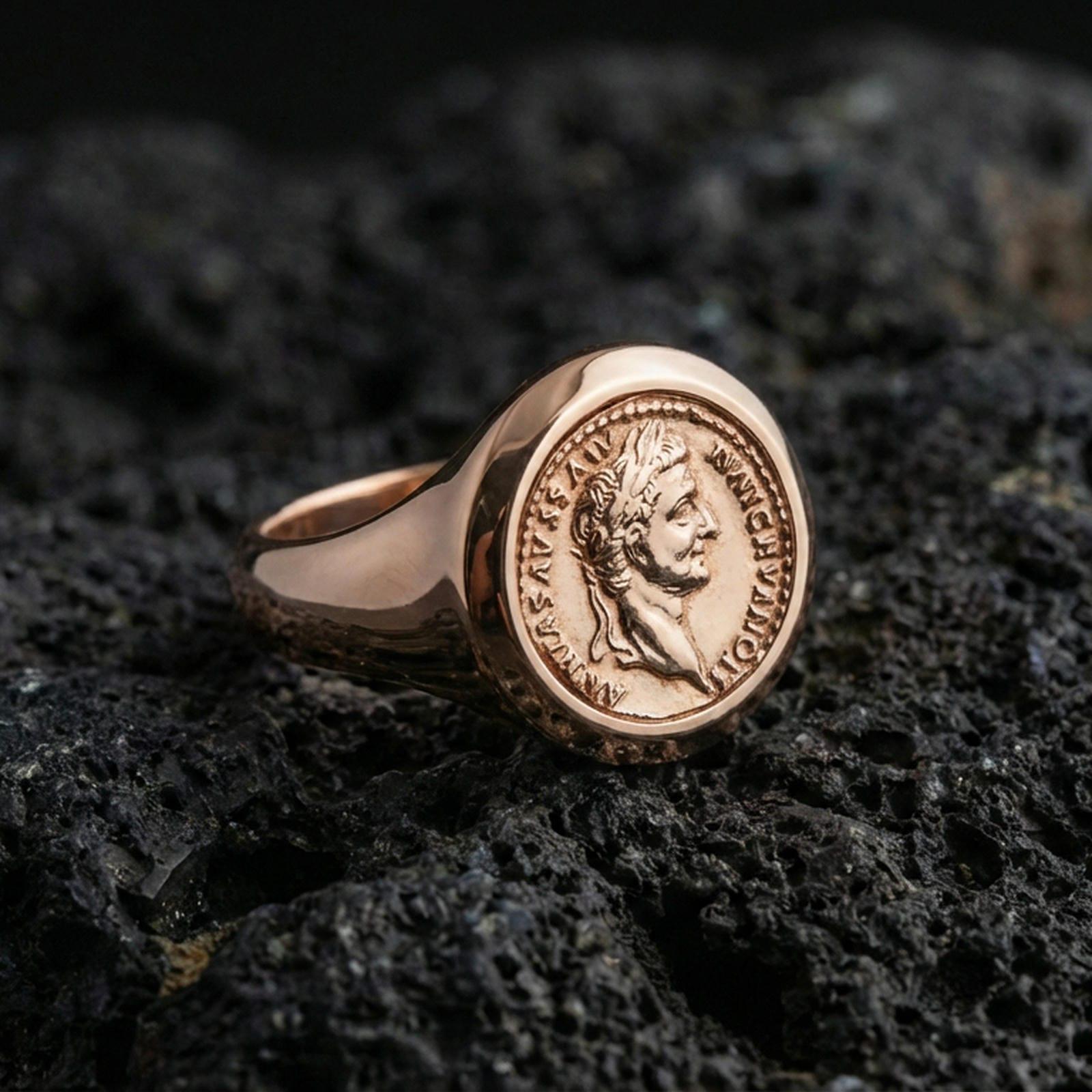 Sterling silver Roman coin signet ring with a rose gold plated finish, classical emperor portrait medallion and ringed border texture, close-up on volcanic rock