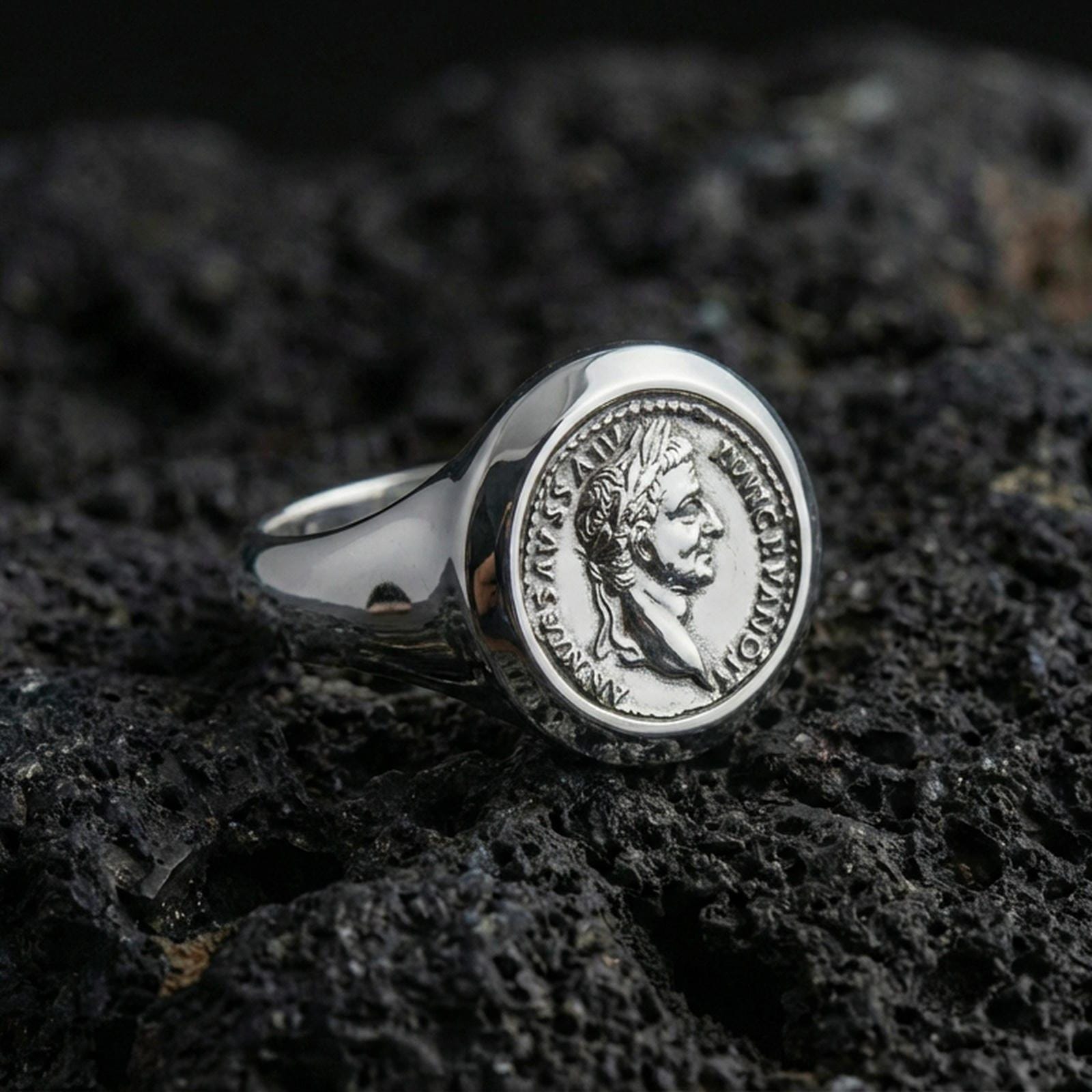 Sterling silver Roman coin signet ring in a polished silver finish, raised imperial portrait seal with circular inscription detail, close-up on volcanic stone