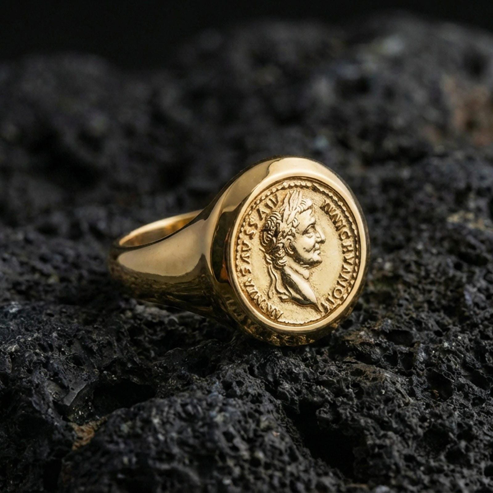 Sterling silver Roman coin signet ring with a gold plated finish, antique coin-style emperor profile and engraved rim text, macro on volcanic rock