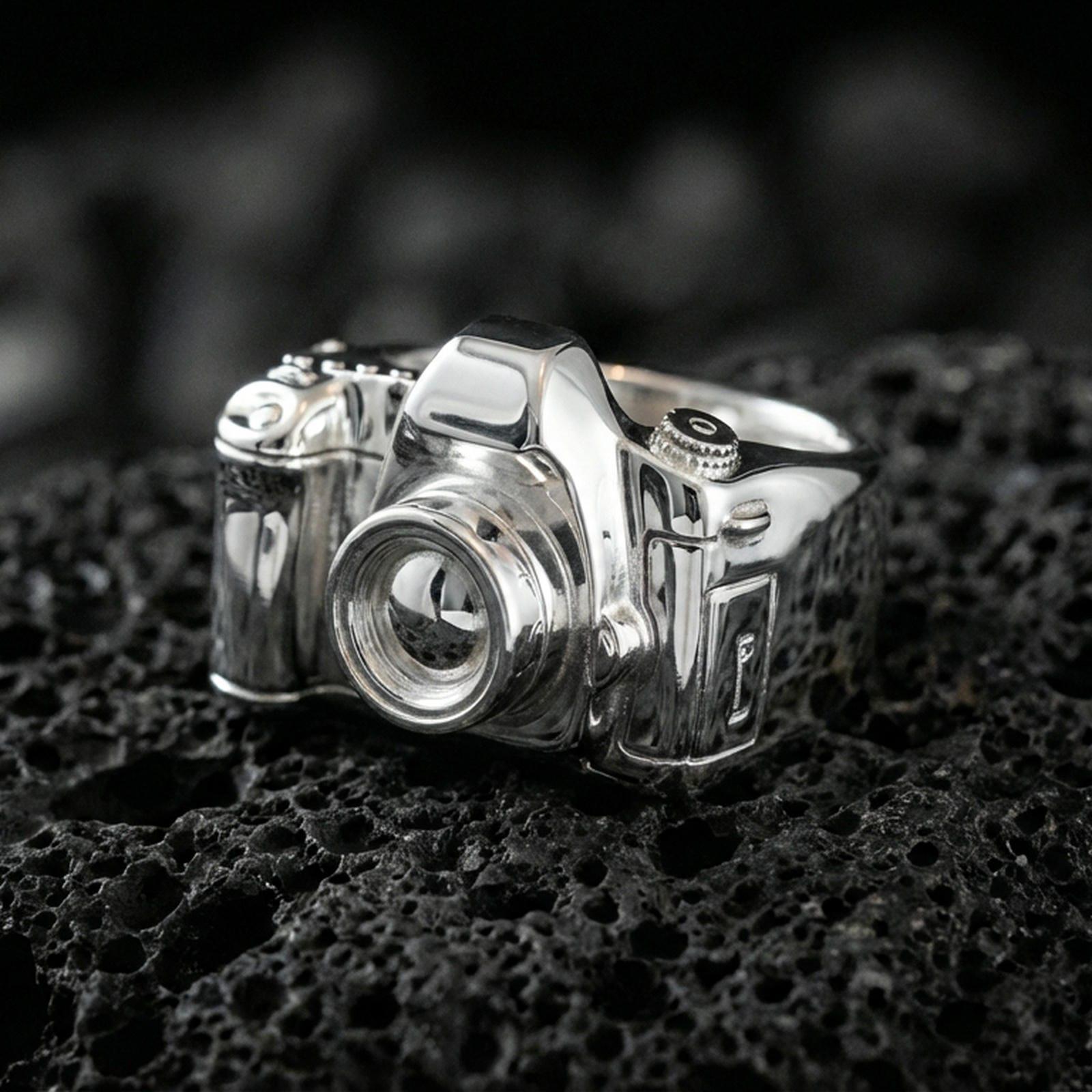 Sterling silver camera signet ring in a polished silver finish, sculpted retro camera body with raised lens and dials, close-up on volcanic stone