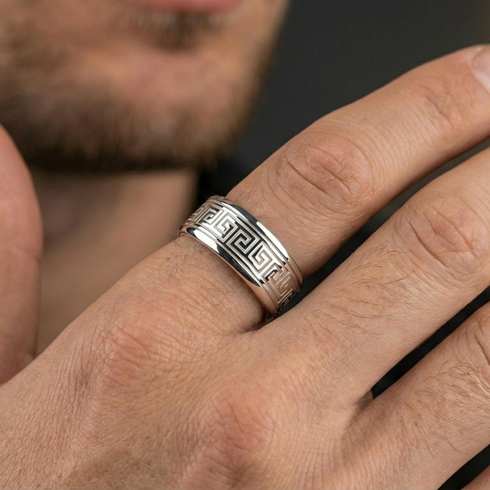 Polished silver Greek key wedding band on finger, crisp geometric meander border engraving, refined everyday wear close-up.