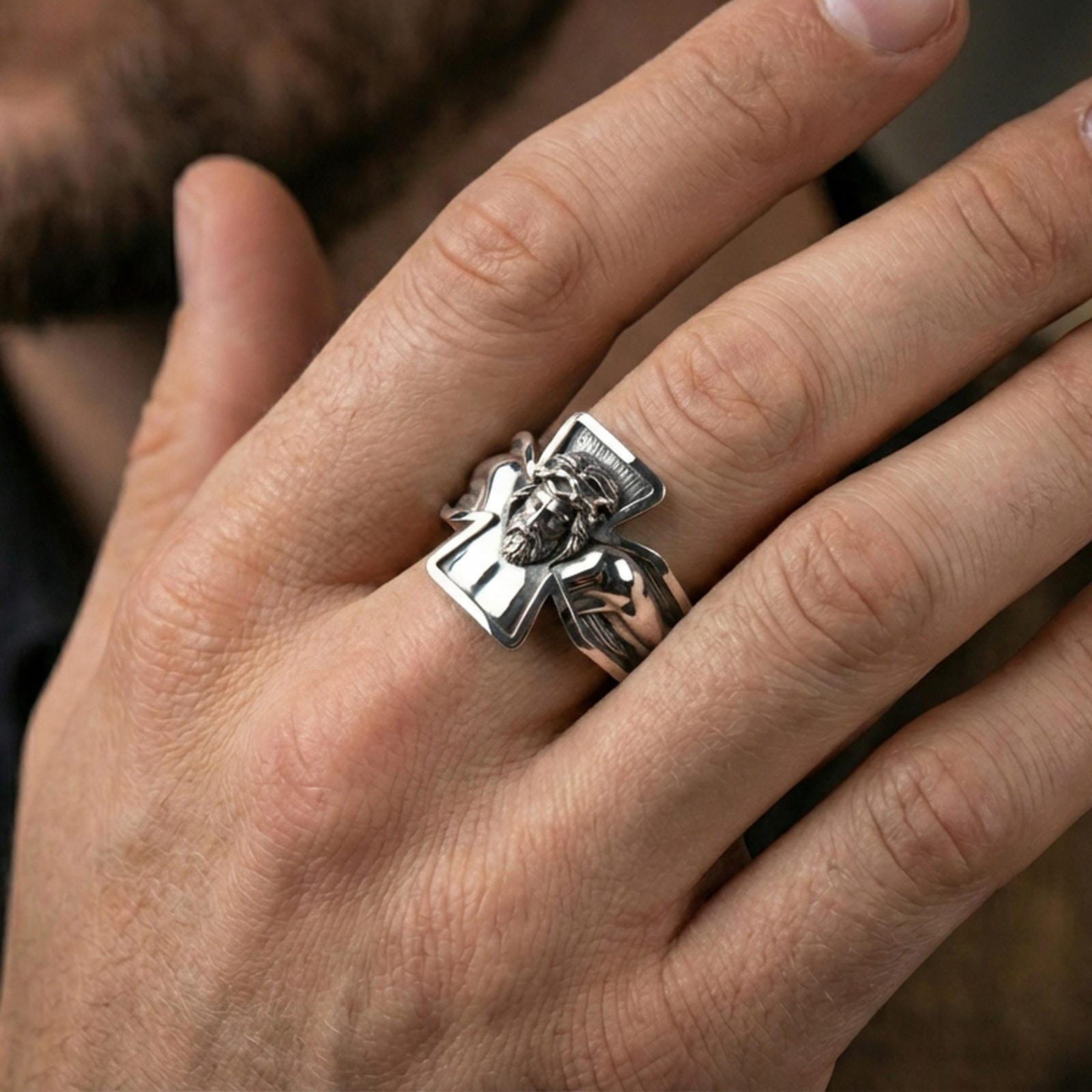 Polished silver Jesus crucifix ring on finger, crisp Christ figure sculpture and cross outline detail, refined everyday wear close-up.