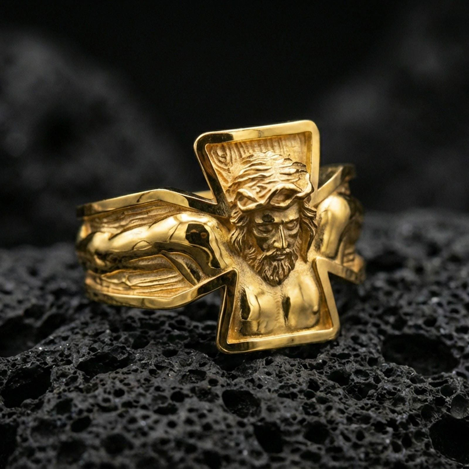 Gold plated sterling silver crucifix Jesus ring on volcanic rock, detailed Christ relief with bold open cross frame, luxury jewelry product photography.