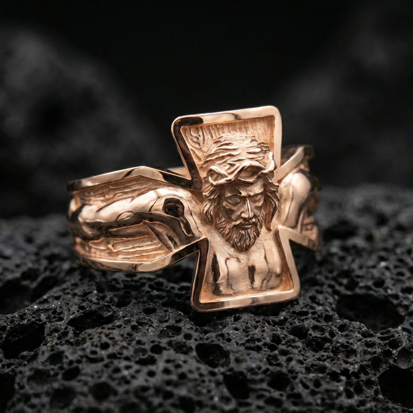 Rose gold plated crucifix Jesus ring on volcanic stone, sculpted Christ figure with deep contrast and sharp cross outline, minimal high-end close-up.